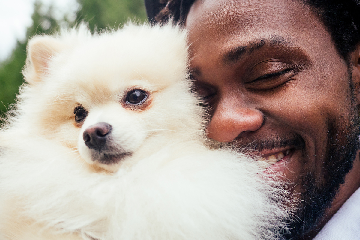 Close-up of African-American man hugging his fluffy white spitz in park.
