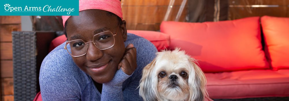 Photo of African-American woman with glasses wearing a blue sweater, lounging with a small white dog