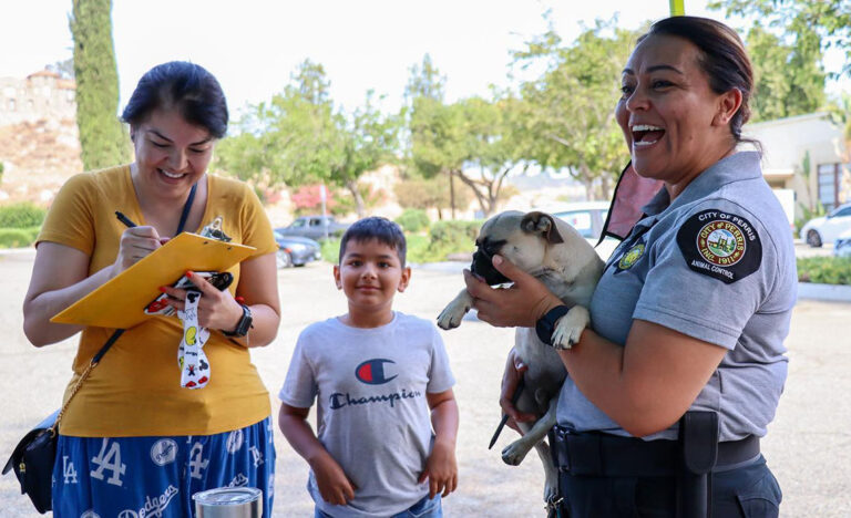 Christina holds a small dog during a spay/neuter event while a woman signs a clipboard and a young boy looks on. Photo credit: City of Perris