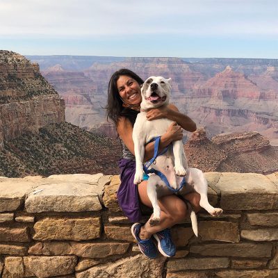 Dianne Prado sitting on a stone wall holding a pitbull with a canyon in the background